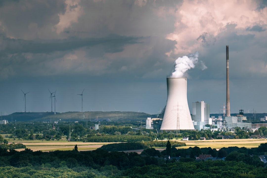 Nuclear power plant cooling tower smoke wind turbines landscape. Large cooling tower emitting steam with modern wind turbines